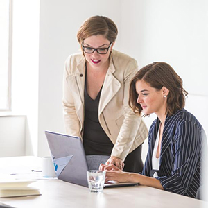 "supervisor assisting her employee with a task on a laptop"