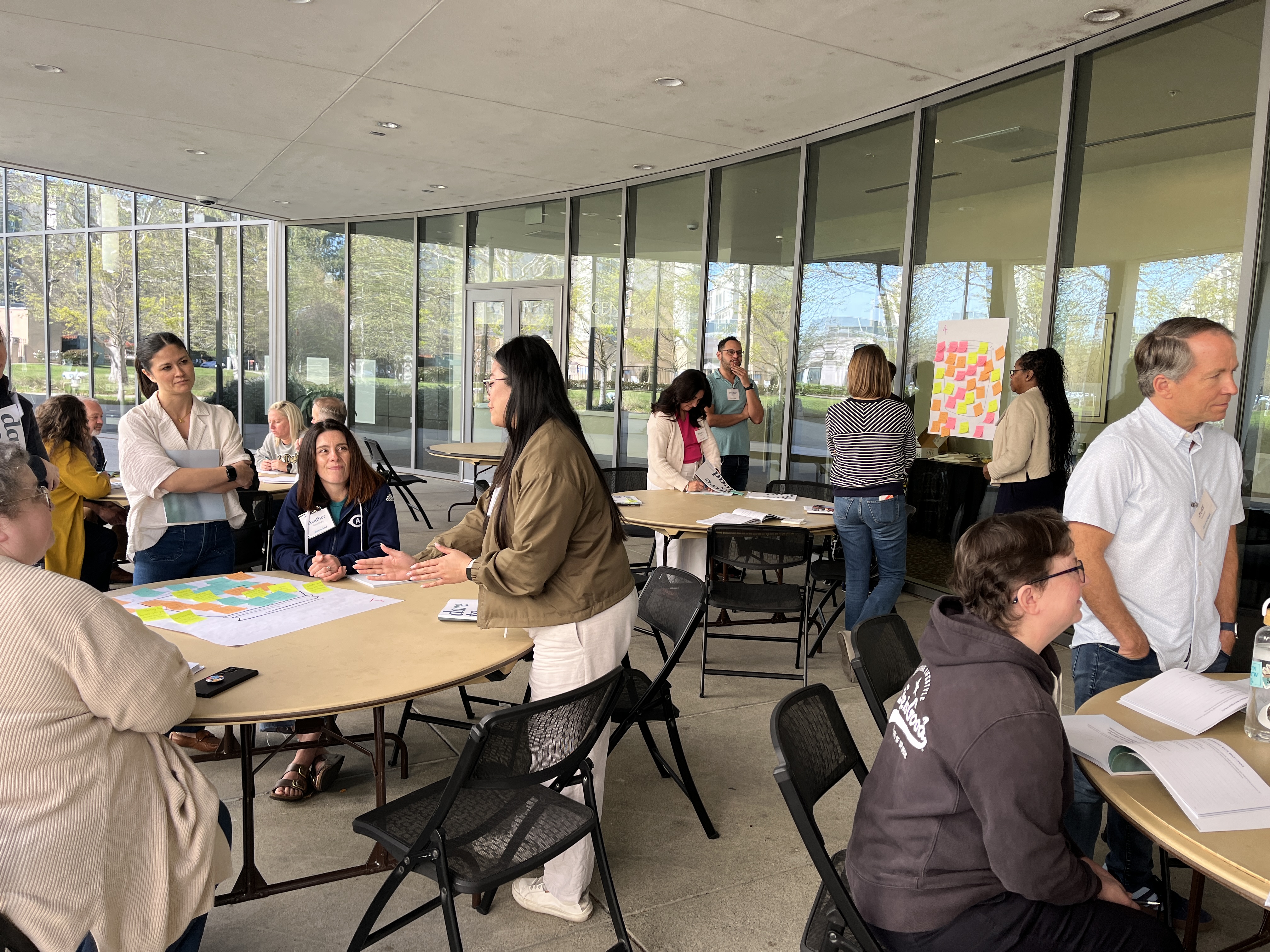 Adults collaborating around round tables in bright glass-walled meeting room