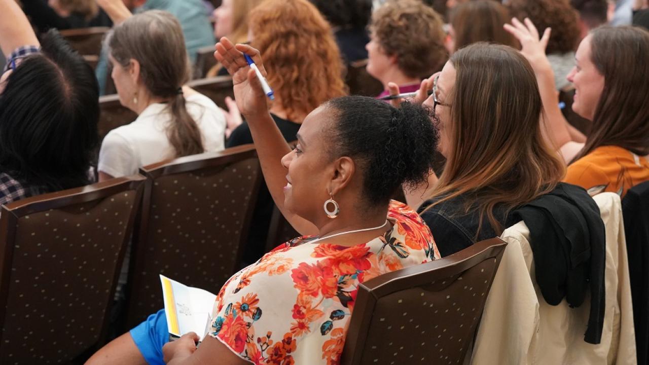 People sitting at a presentation with their hands raised.