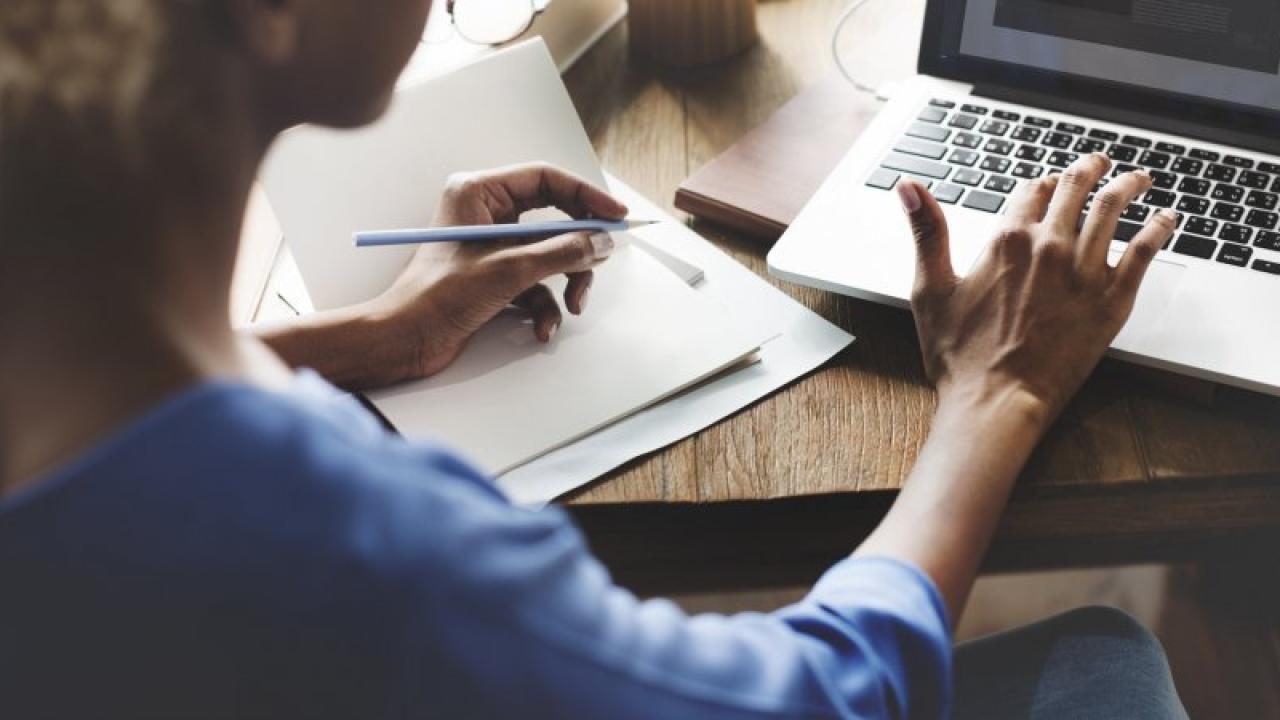 Person sitting in front of laptop taking notes on a piece of paper. 