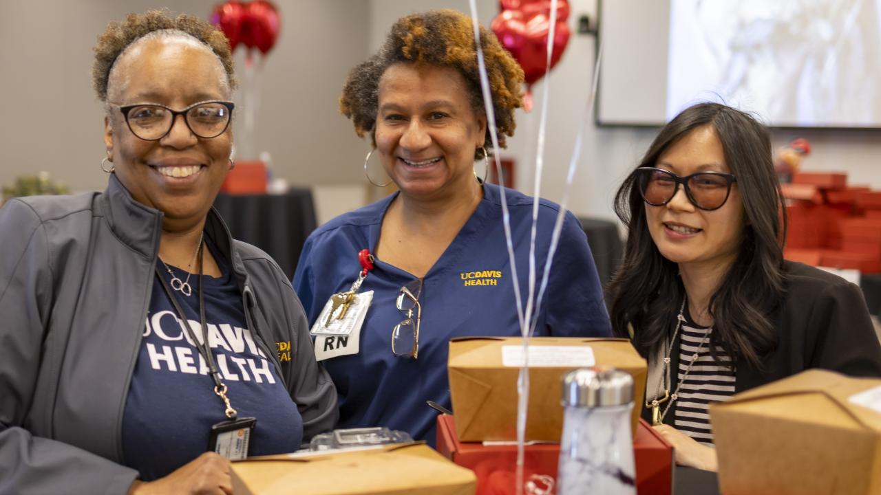 Three women celebrating at a table, surrounded by heart balloons.