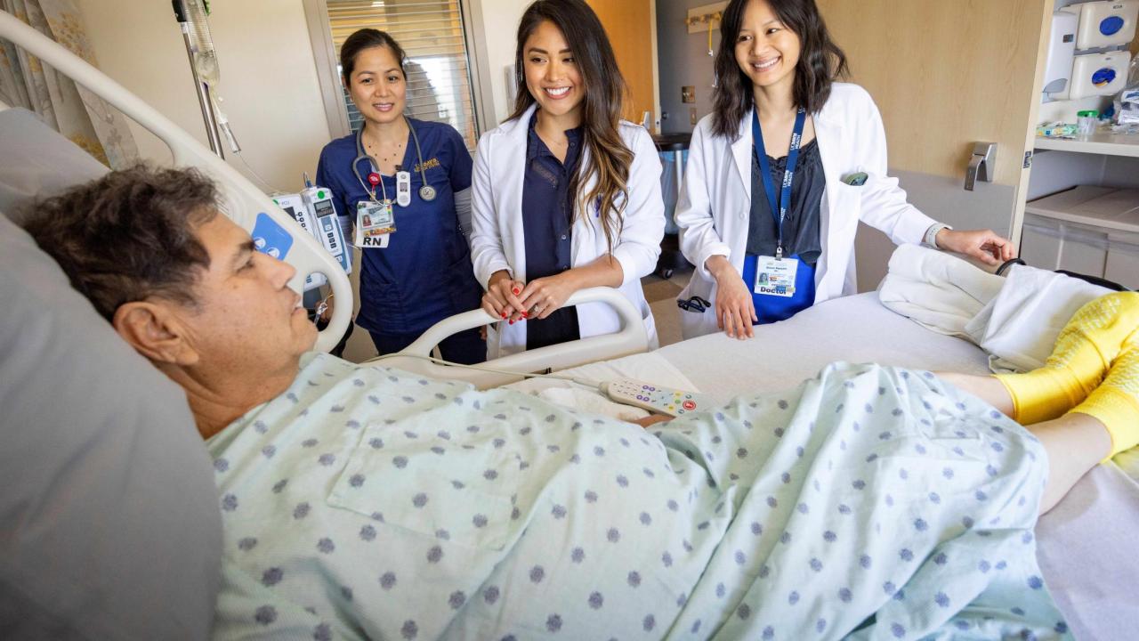 Three female medical staff standing next a male patient's bed.