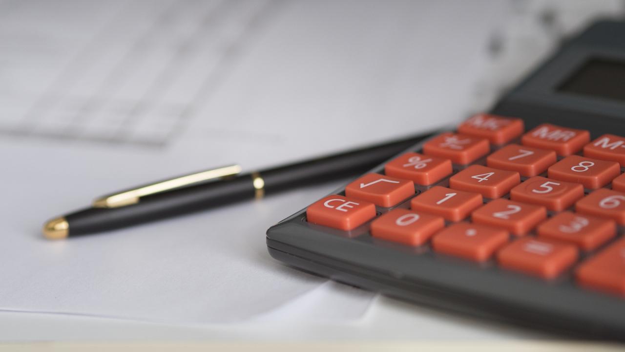 A close-up of an orange calculator and a black pen on white paper with printed graphs.