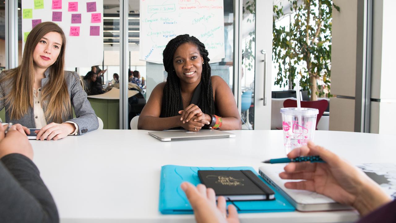 two female colleagues listening to another coworker across a conference table