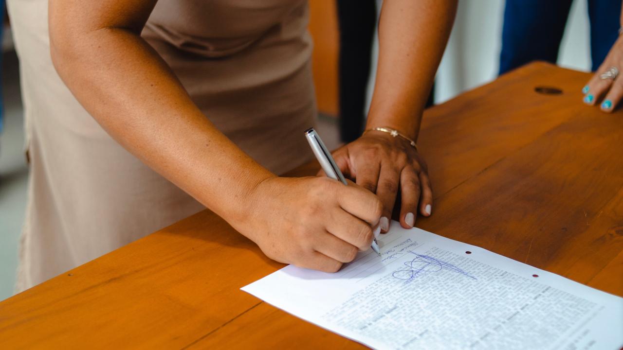Person signing a paper on a wooden table 