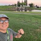 Selfie of smiling person in cap and glasses by park pond. 