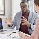 A man in glasses gestures while discussing data on a laptop with a woman.