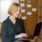 An older woman holds a laptop while sitting.