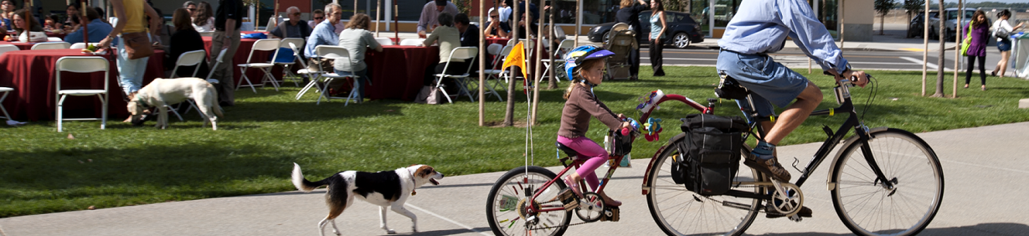 men and his daughter riding bikes with their dog running behind